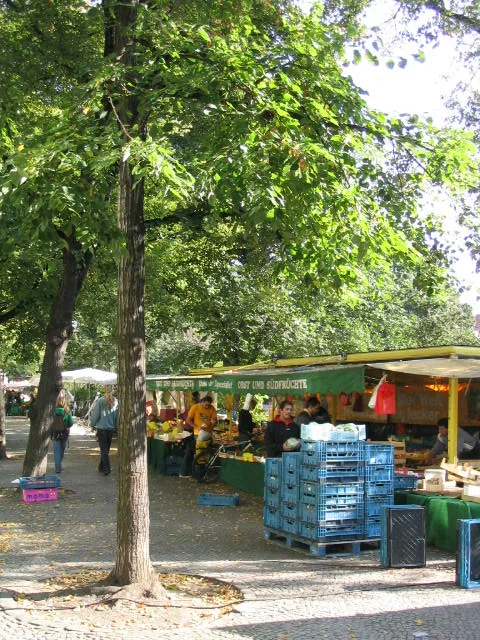 Het drukke Boxhagener Platz in Friedrichshain Berlijn op een zonnige zaterdag met marktkramen, terrasjes en kastanjebomen